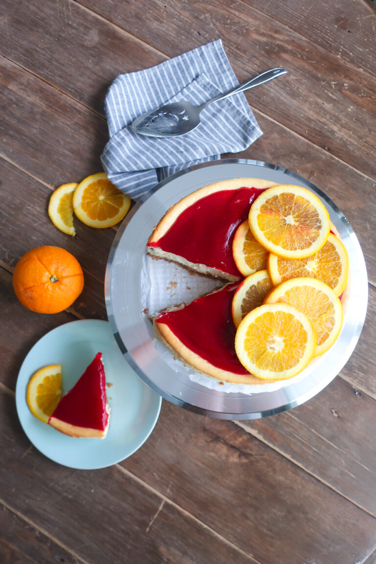 slice and inside look at orange cheesecake with cinnamon spiced graham cracker crust and topped with cranberry sauce