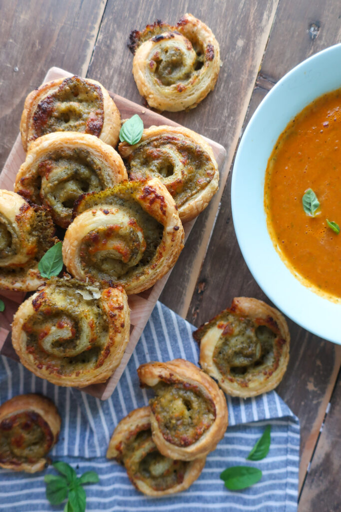 pesto pinwheels made with puff pastry next to a bowl of tomato soup