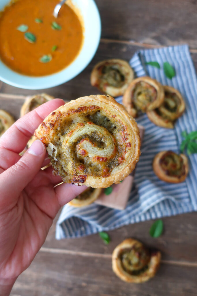 close up of pesto pinwheels made with puff pastry next to a bowl of tomato soup