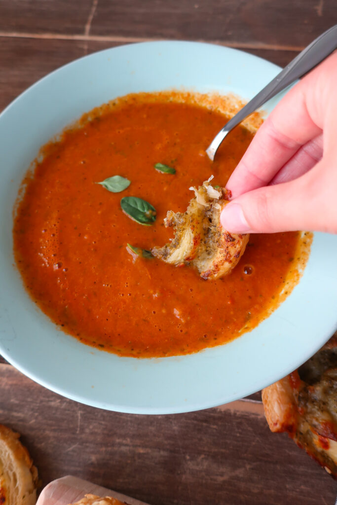 bite of pesto pinwheels made with puff pastry dipped into a bowl of tomato soup