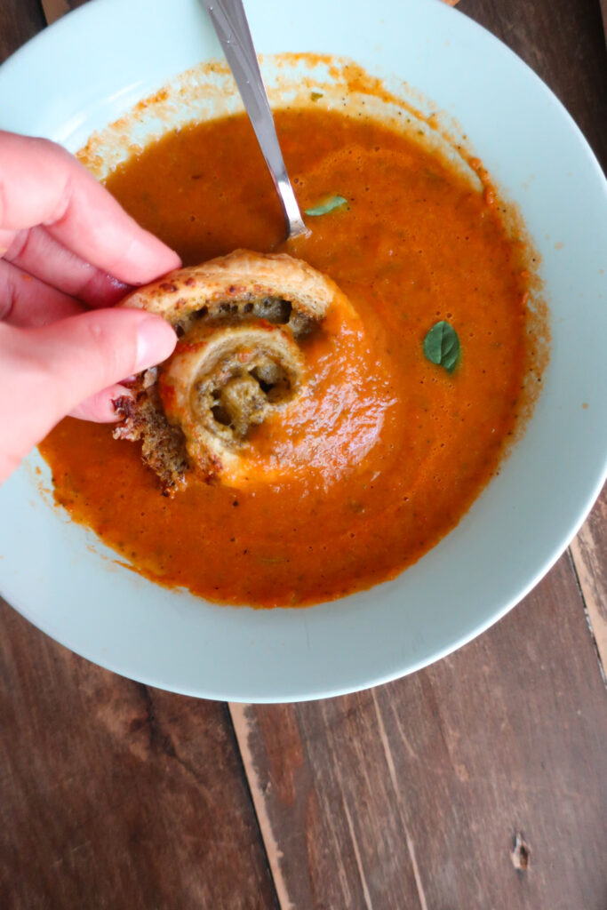 bite of pesto pinwheels made with puff pastry dipped into a bowl of tomato soup