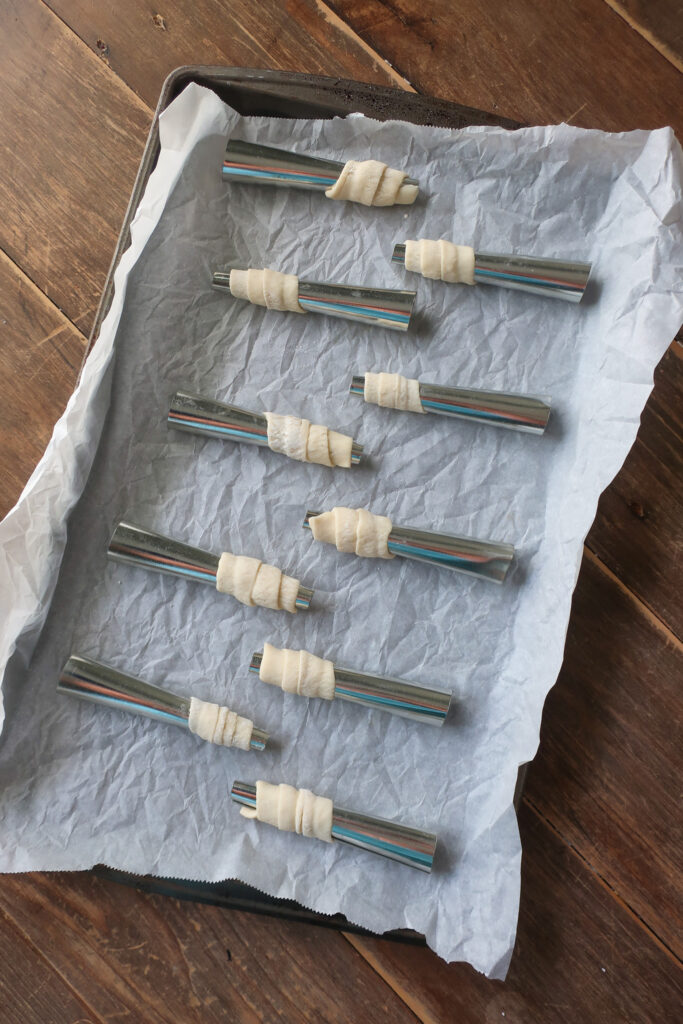 raw puff pastry wrapped on dowel rods for lady lock puff pastry filled with cream frosting