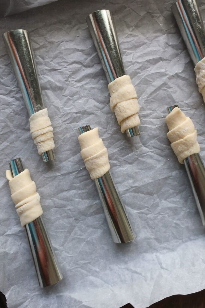 raw puff pastry wrapped on dowel rods for lady lock puff pastry filled with cream frosting