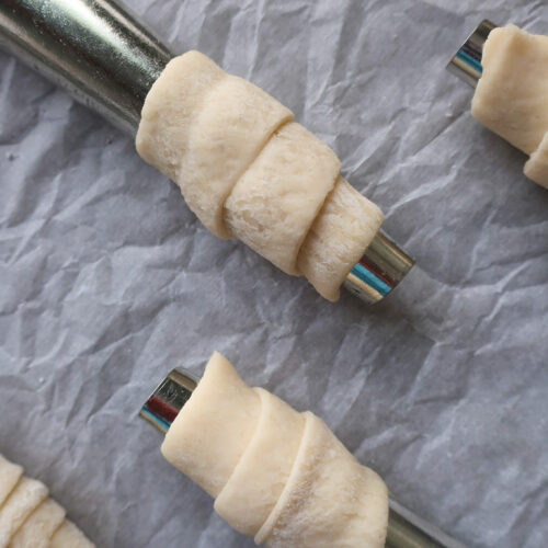 raw puff pastry wrapped on dowel rods for lady lock puff pastry filled with cream frosting