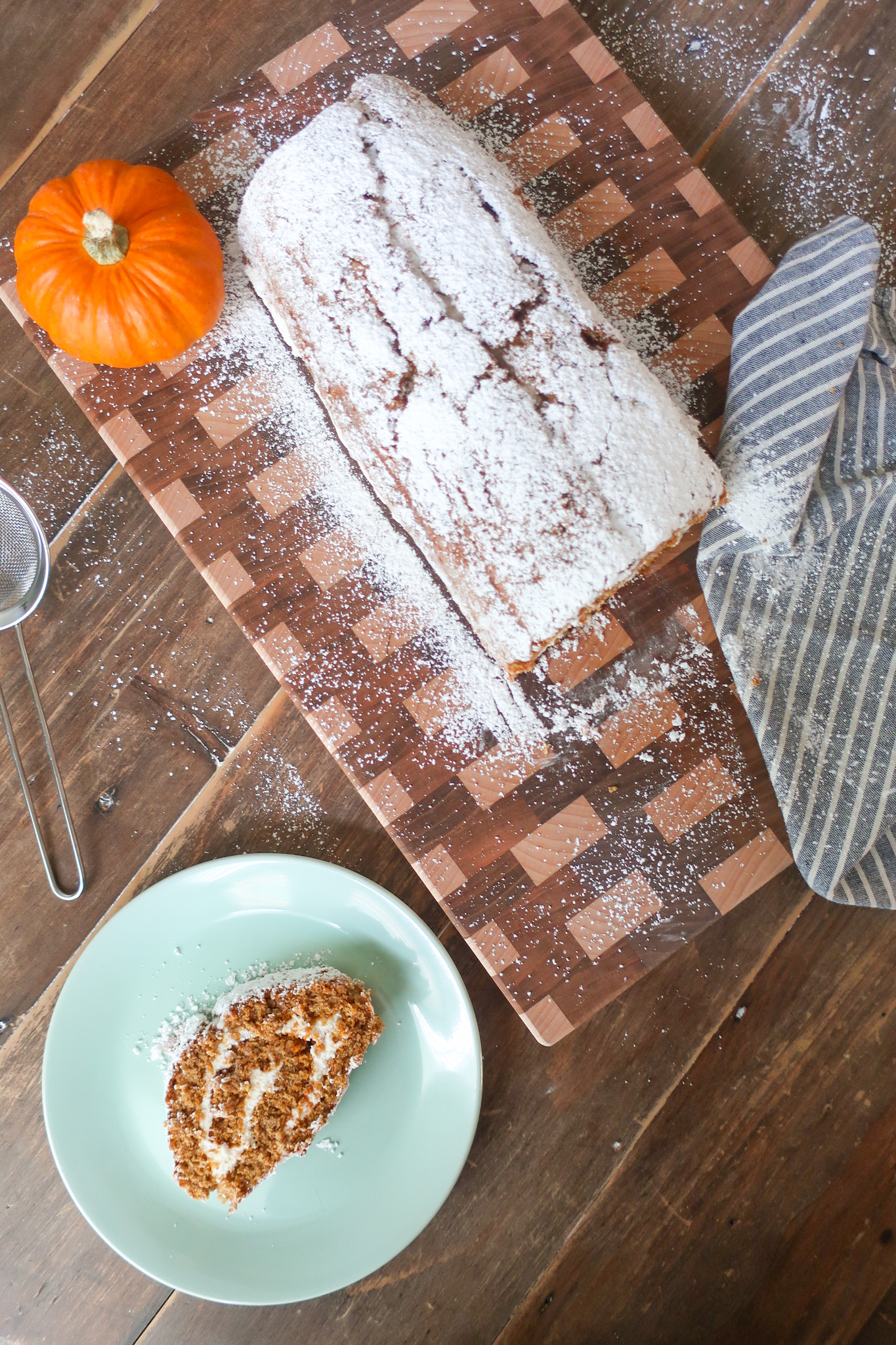 pumpkin cake roll with whipped cream cheese frosting with slice on a plate nearby