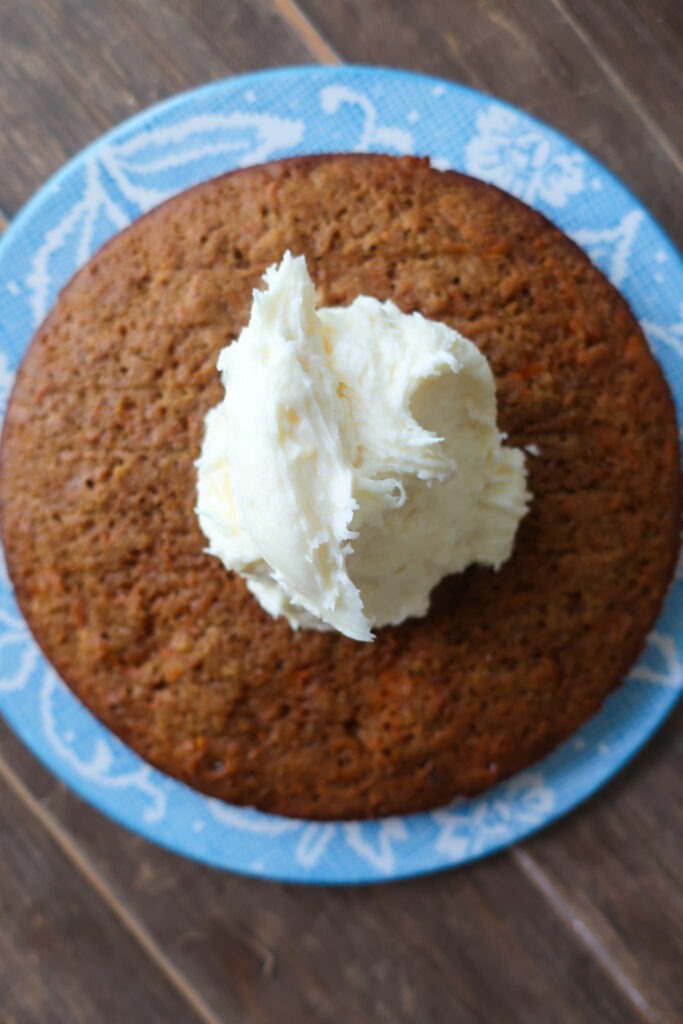 bottom tier of baked carrot cake with plop of frosting on top