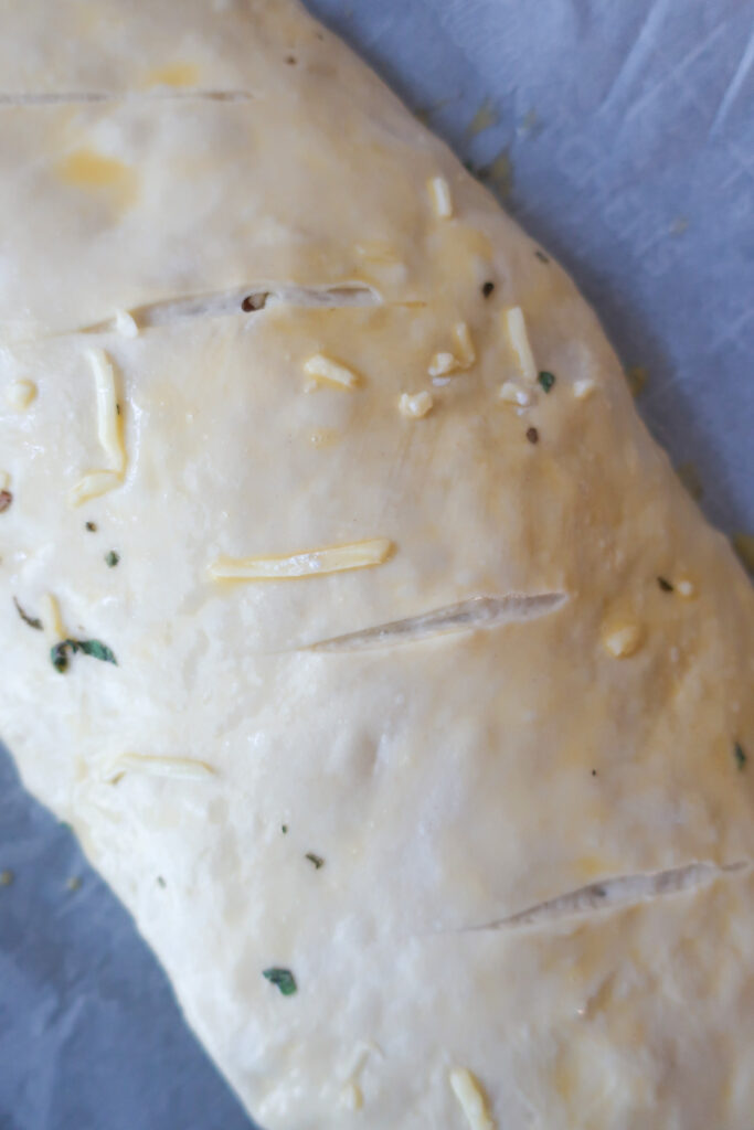 uncooked stromboli wrapped up, with egg wash and slits cut across top