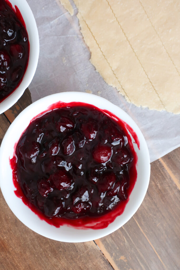 dough for lattice top crust of cherry pie next to bowl of cherry pie filling