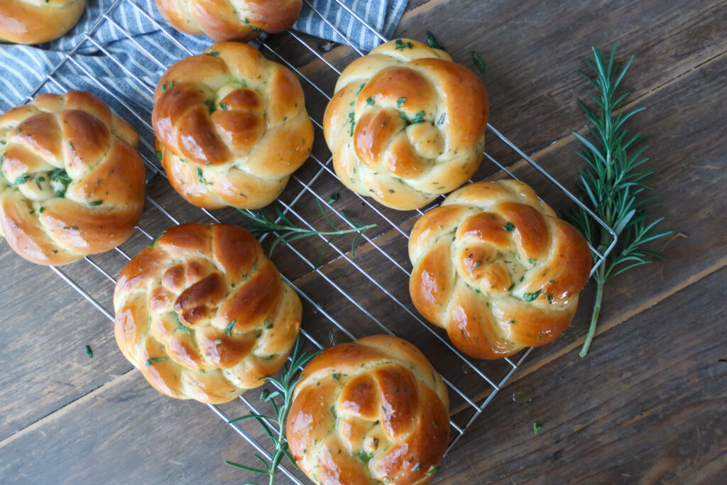 rosemary challah rolls baked and cooling on wire rack on top of blue striped napkin and surrounded by rosemary sprigs