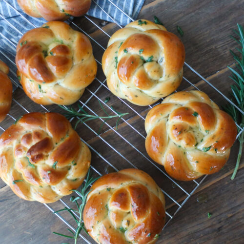 rosemary challah rolls baked and cooling on wire rack on top of blue striped napkin and surrounded by rosemary sprigs