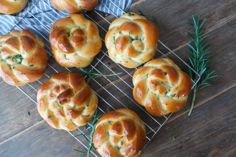 rosemary challah rolls baked and cooling on wire rack on top of blue striped napkin and surrounded by rosemary sprigs