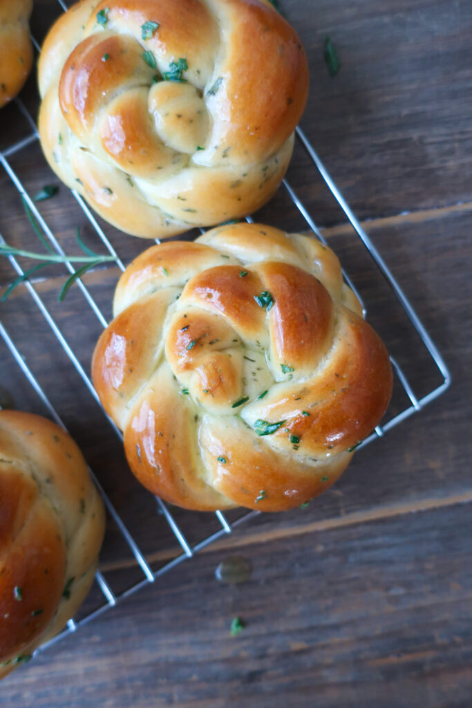 rosemary challah rolls baked and cooling on wire rack on top of blue striped napkin and surrounded by rosemary sprigs