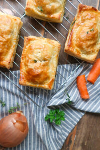 chicken hand pies on wire rack surrounded by herbs, carrots, onion, and a striped blue napkin