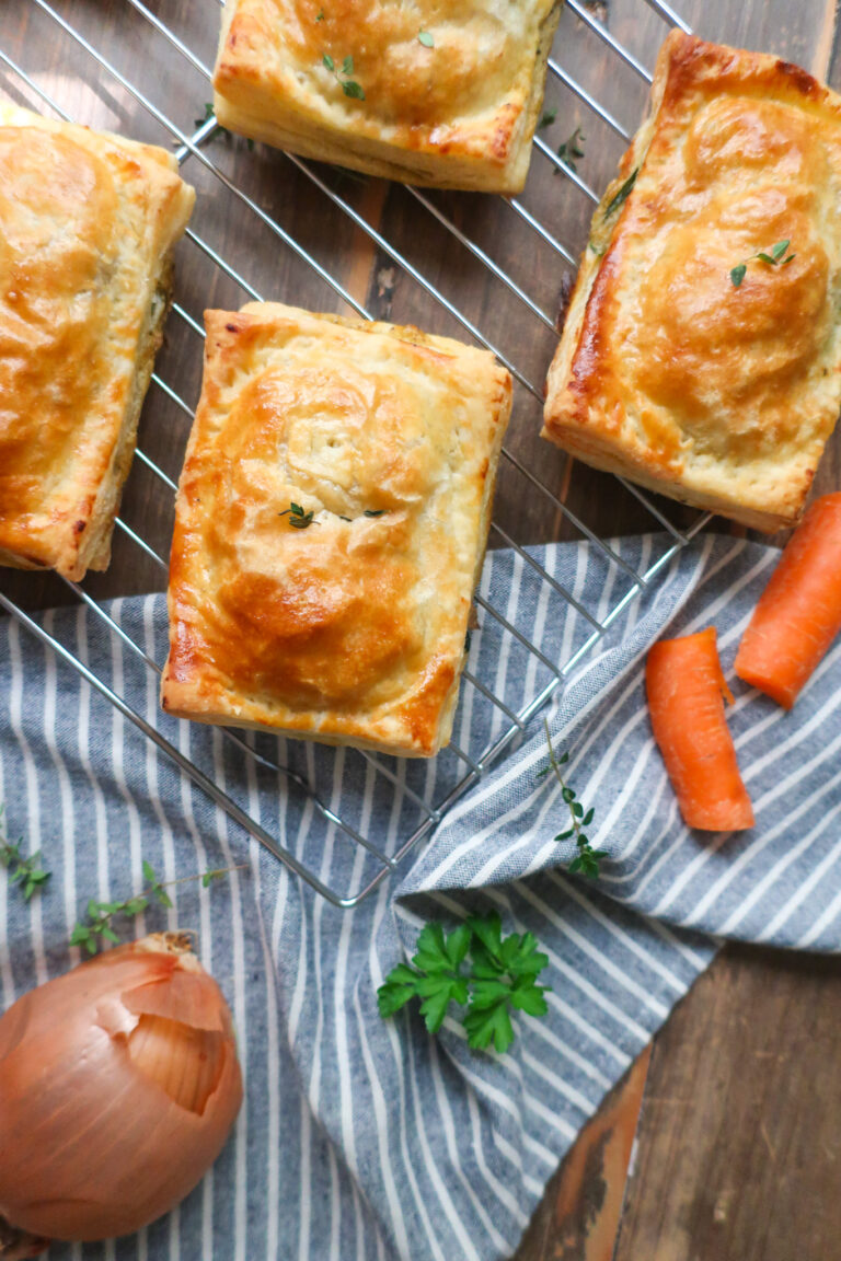 chicken hand pies on wire rack surrounded by herbs, carrots, onion, and a striped blue napkin