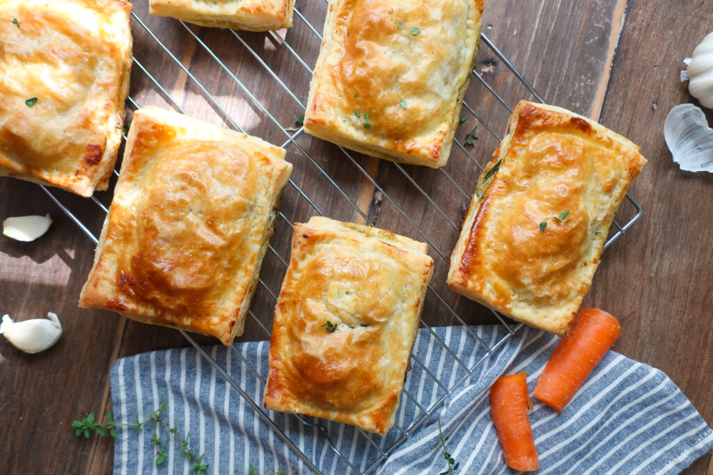 chicken hand pies on wire rack surrounded by herbs, carrots, onion, and a striped blue napkin