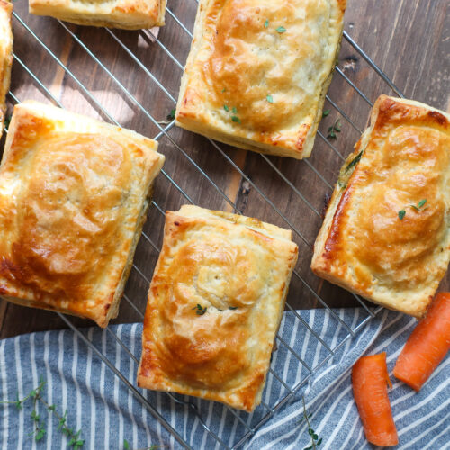 chicken hand pies on wire rack surrounded by herbs, carrots, onion, and a striped blue napkin