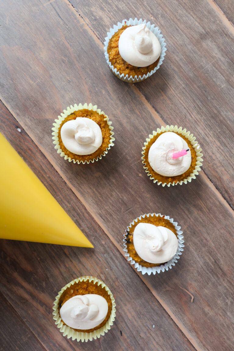 blueberry and pumpkin. pupcakes (dog cupcakes) with peanut butter and greek yogurt frosting; cupcakes sitting on wood table with yellow party hat