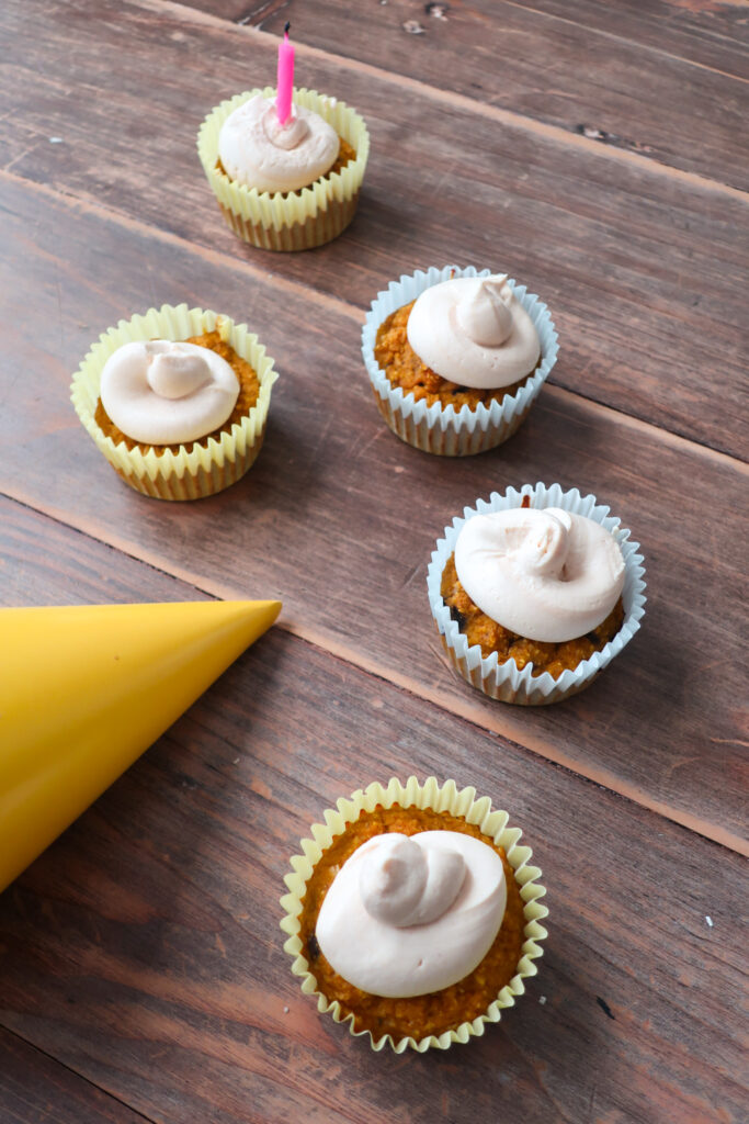 blueberry and pumpkin. pupcakes (dog cupcakes) with peanut butter and greek yogurt frosting; cupcakes sitting on wood table with yellow party hat