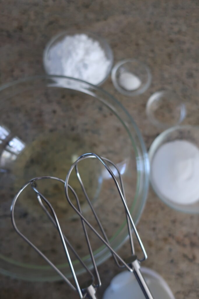 ingredients for french meringue; egg whites in mixing bowl; hand mixer; individual pavlovas with berry compote and fresh whipped cream