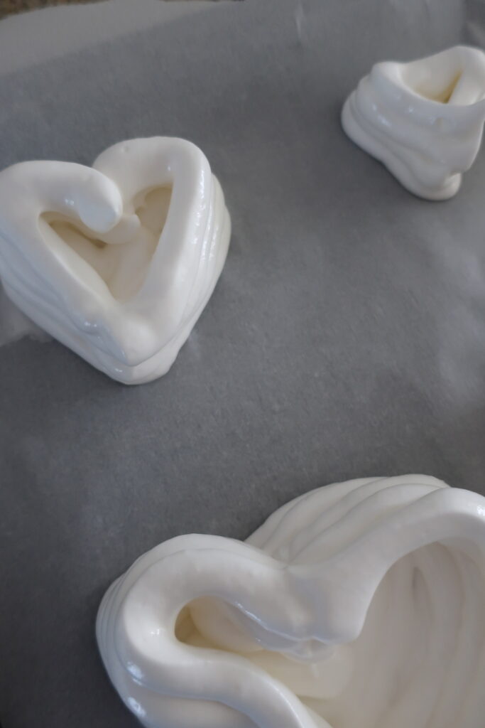 baked pavlovas made with french meringue and piped into heart shapes; individual pavlovas with berry compote and fresh whipped cream; valentine's dessert