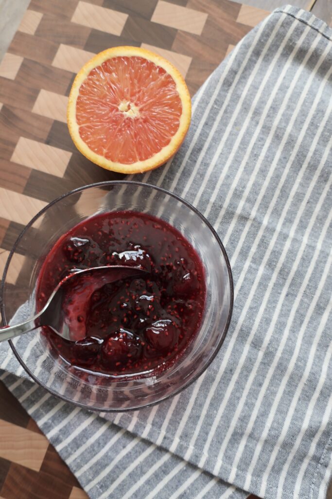 bowl of cherry berry compote on blue napkin with half of orange