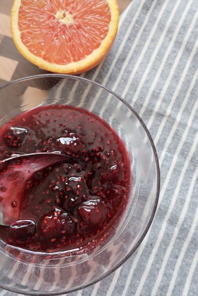 bowl of cherry berry compote on blue napkin with half of orange