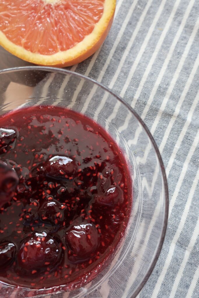 bowl of cherry berry compote on blue napkin with half of orange