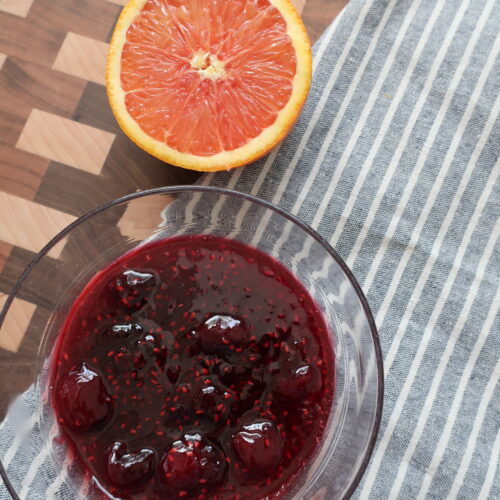 bowl of cherry berry compote on blue napkin with half of orange