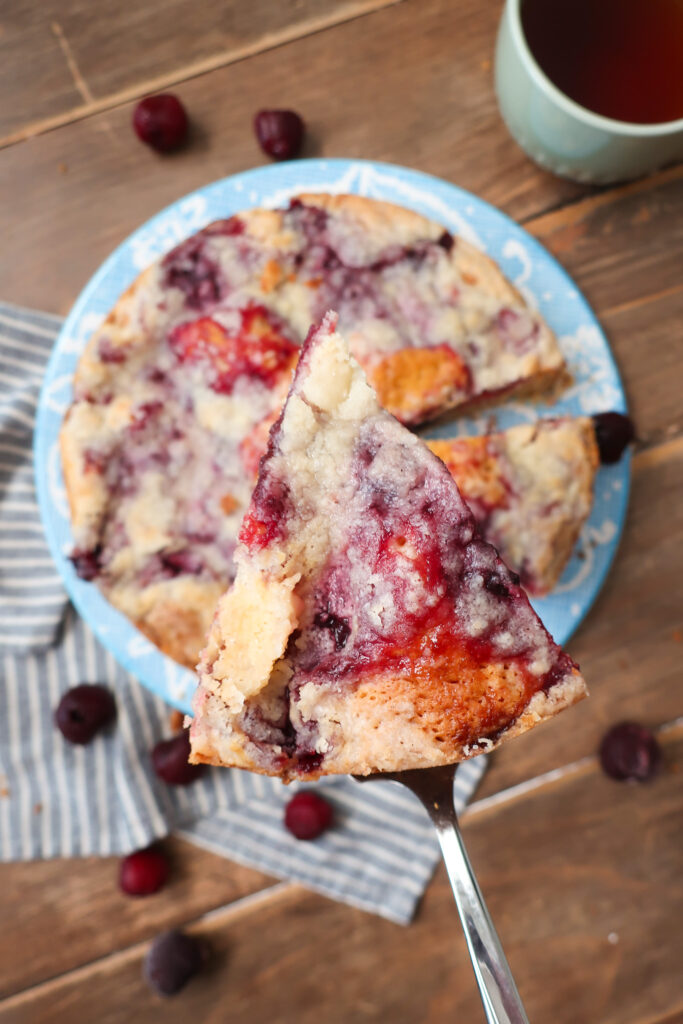 cherry coffee cake, coffee cake with cherry topping and streusel crumble, cherry coffee cake next to mug of hot drink, coffee cake next to mug of coffee