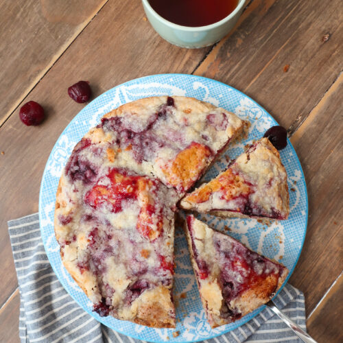 cherry coffee cake, coffee cake with cherry topping and streusel crumble, cherry coffee cake next to mug of hot drink, coffee cake next to mug of coffee