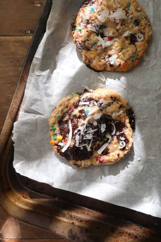 baked cookies on baking tray in sunshine; dark chocolate oat sea salt cookies; dark chocolate coconut cookies; dark chocolate chip cookies with sprinkles; measuring cup filling with traditional oats