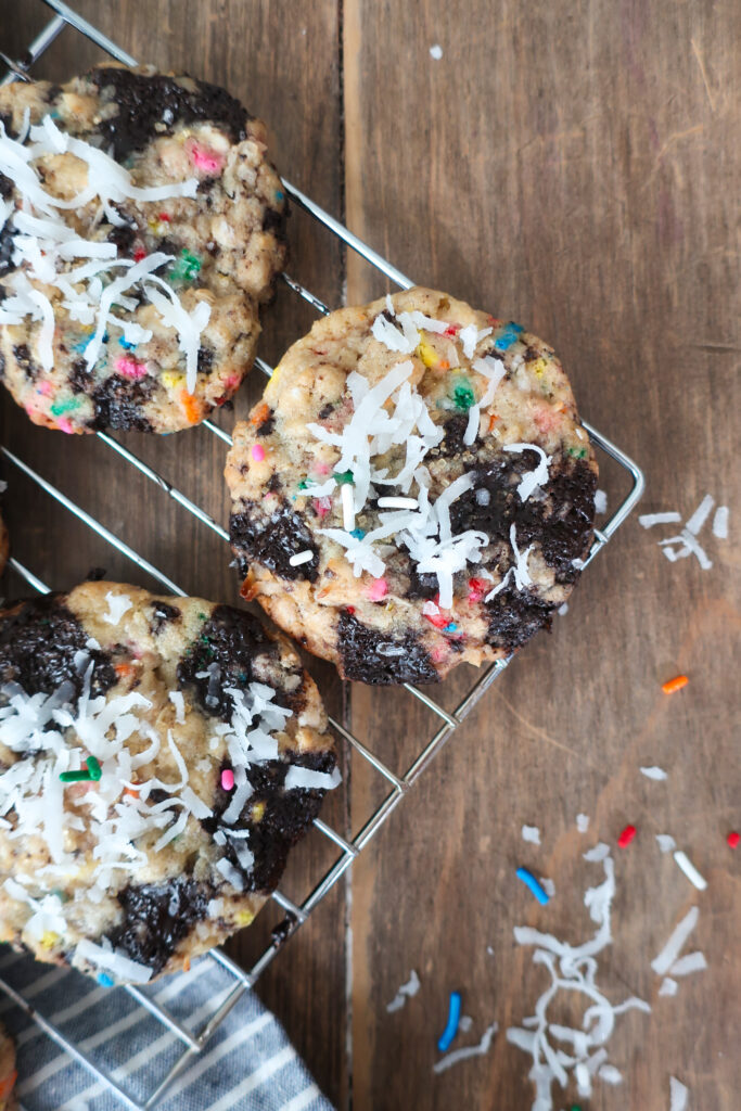 baked cookies on baking tray in sunshine; dark chocolate oat sea salt cookies; dark chocolate coconut cookies; dark chocolate chip cookies with sprinkles; measuring cup filling with traditional oats