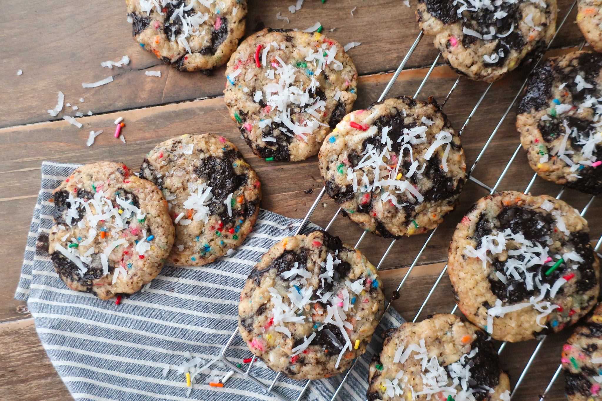 baked cookies on baking tray in sunshine; dark chocolate oat sea salt cookies; dark chocolate coconut cookies; dark chocolate chip cookies with sprinkles; measuring cup filling with traditional oats