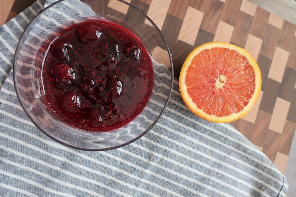 bowl of cherry berry compote on blue napkin with half of orange