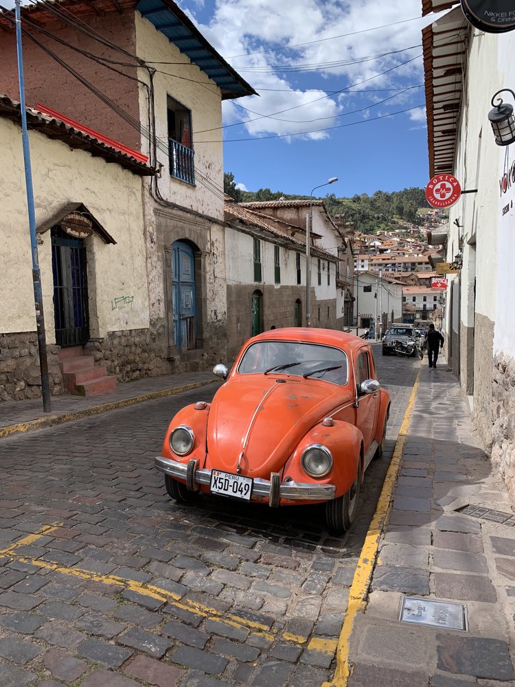 orange volkswagen beetle on cobblestone streets of cusco in peru, south america; solo female travel; solo backpacking; backpacking south america; backpacking tips; peru itinerary;