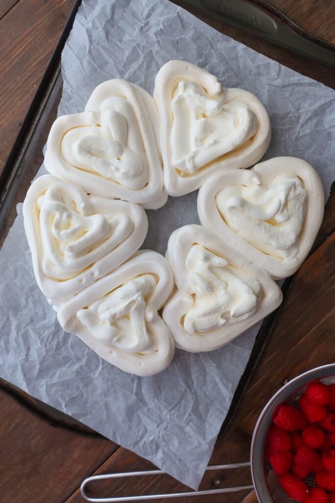 baked french meringue piped into hearts and filled with fresh whipped cream for pavlova hearts wreath with french meringue, piped into heart baskets and filled with fresh whipped cream and fresh raspberries