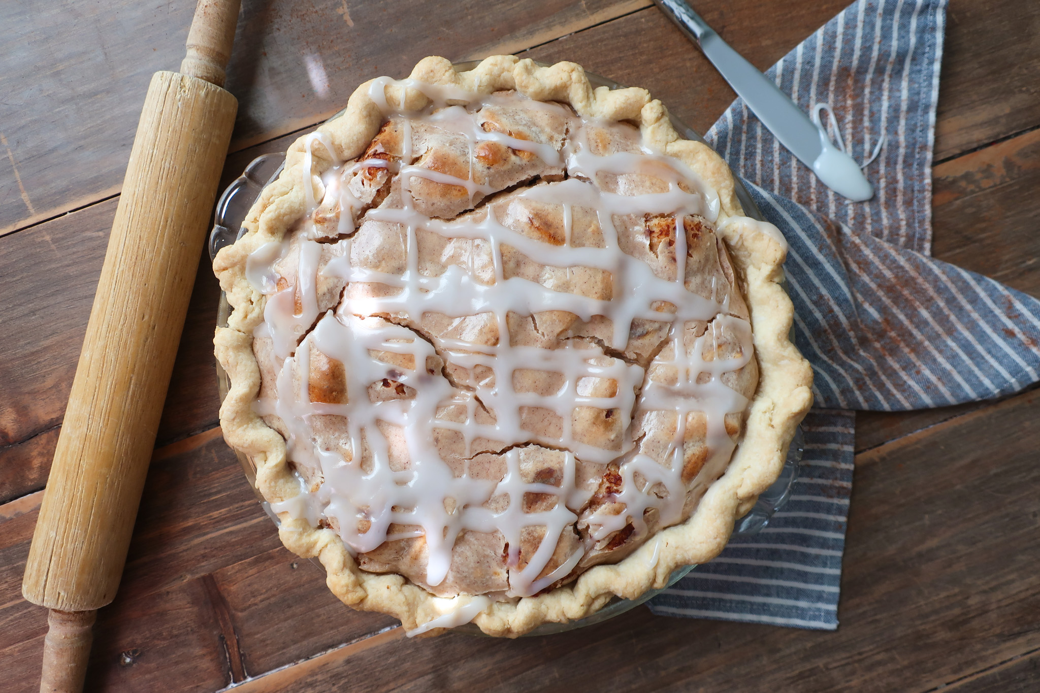 easy cinnamon roll pie with cream cheese filling, baked cinnamon pie on striped blue and white napkin on wooden table with rolling pin nearby