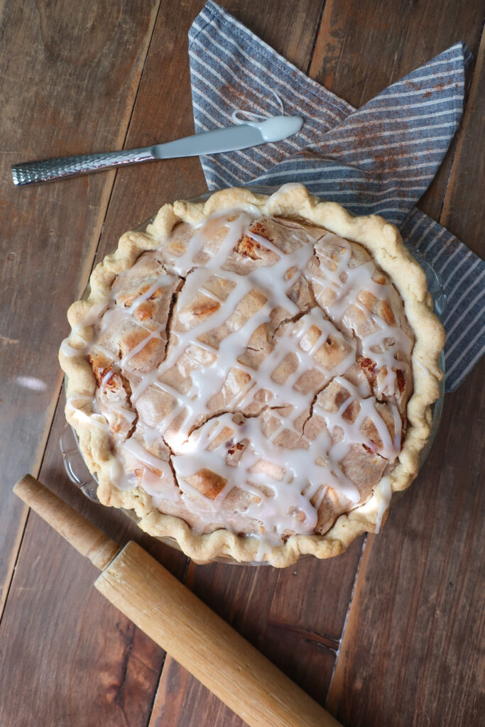 easy cinnamon roll pie with cream cheese filling, baked cinnamon pie on striped blue and white napkin on wooden table with rolling pin nearby