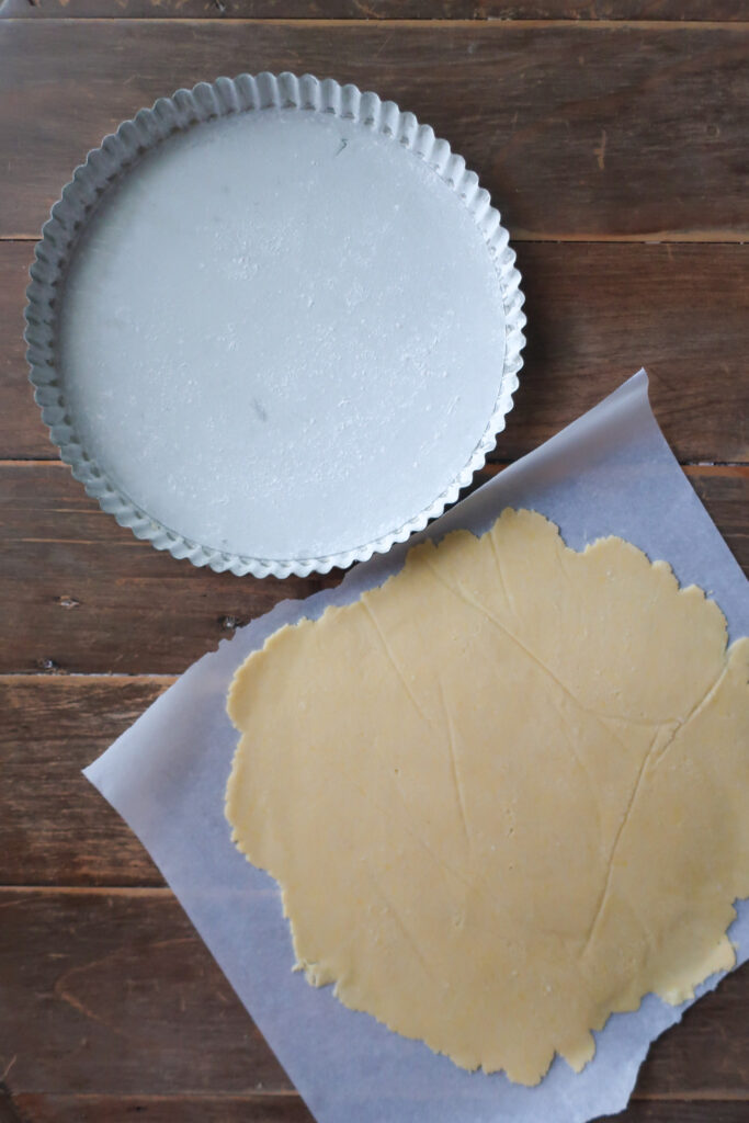 rolled dough of pastry crust on parchment paper next to floured tart pan for chocolate toffee tart