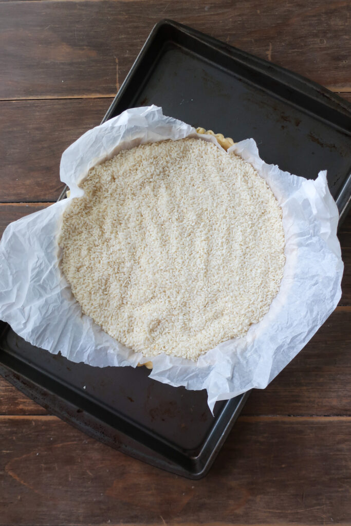 unbaked pastry crust in tart pan filled with rice for blind baking for chocolate toffee tart