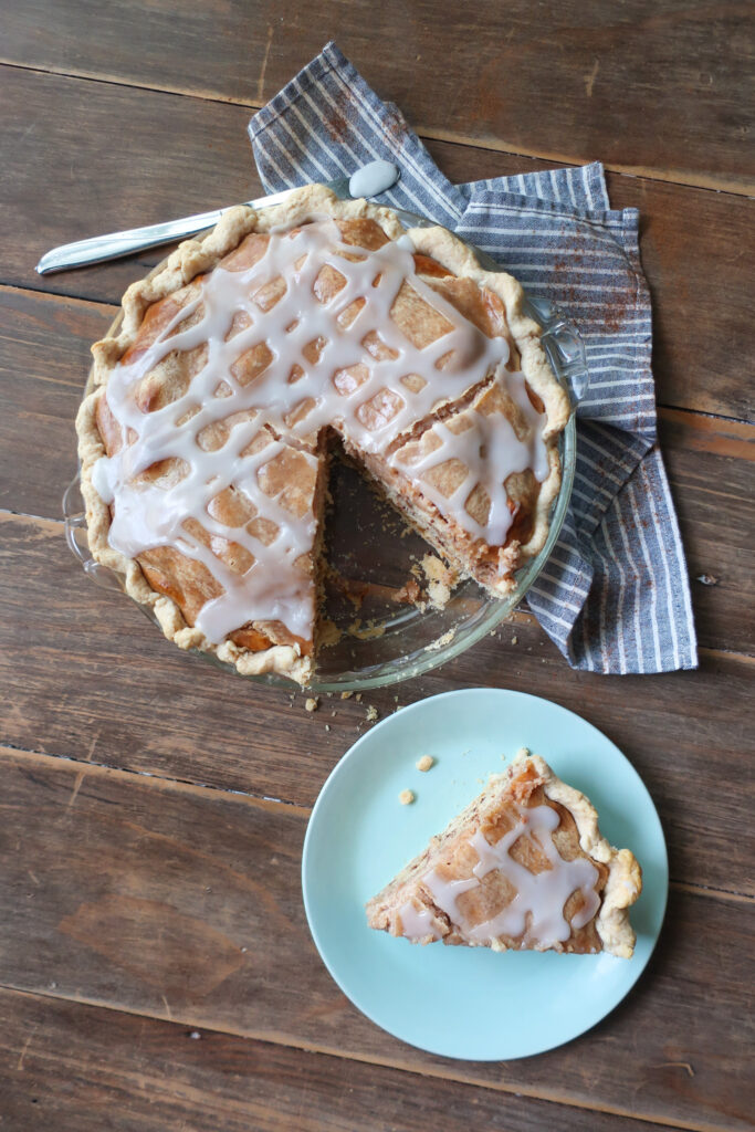 easy cinnamon roll pie with cream cheese filling, baked cinnamon pie on striped blue and white napkin on wooden table, slice of easy cinnamon roll pie with cream cheese filling