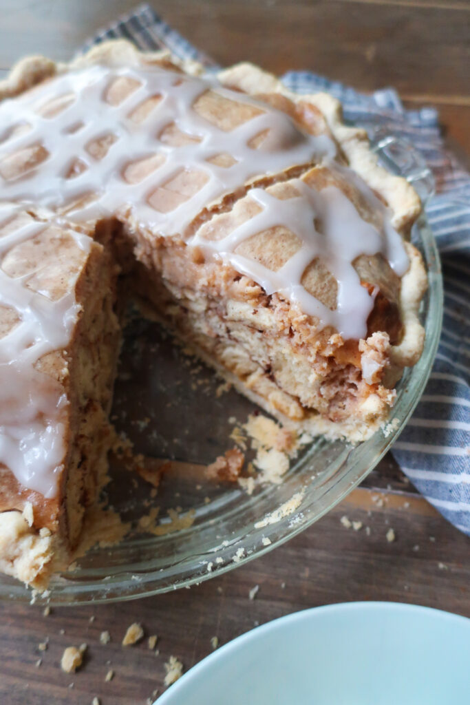 easy cinnamon roll pie with cream cheese filling, baked cinnamon pie on striped blue and white napkin on wooden table, slice of easy cinnamon roll pie with cream cheese filling