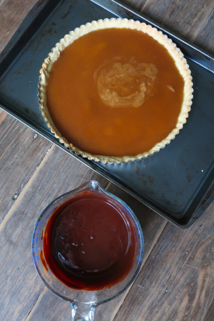 baked pastry crust filled with toffee layer next to bowl of bittersweet chocolate ganache for chocolate toffee tart