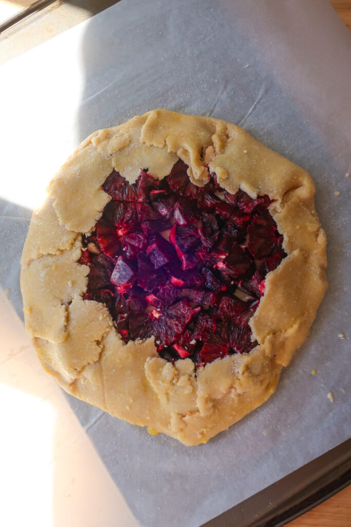 raw pie crust dough wrapped around layers of sweetened cream cheese and blood oranges to make a galette, unbaked blood orange galette drizzled with homemade salted caramel