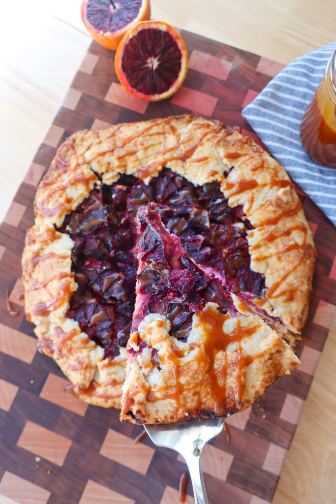 slice of citrus galette, galette topped with salted caramel, cut blood oranges next to galette, blood orange galette drizzled with homemade salted caramel