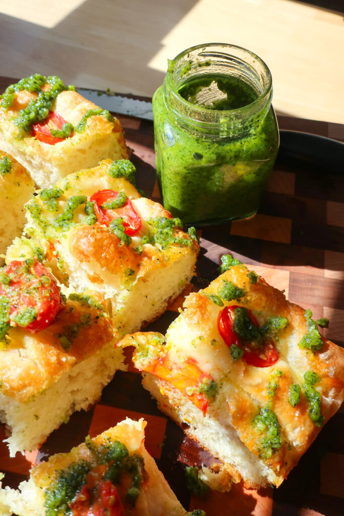 jar of pesto on wooden cutting board, no-knead focaccia, one focaccia two flavors, tomato pesto focaccia, strawberry cheesecake focaccia