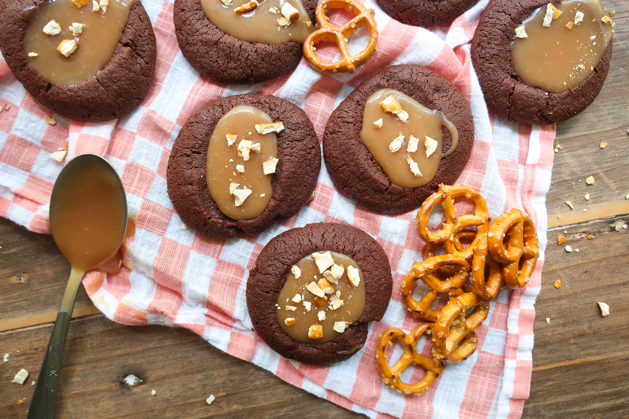 salted caramel pretzel chocolate shortbread thumbprint cookies next to mini pretzels and spoon of salted caramel