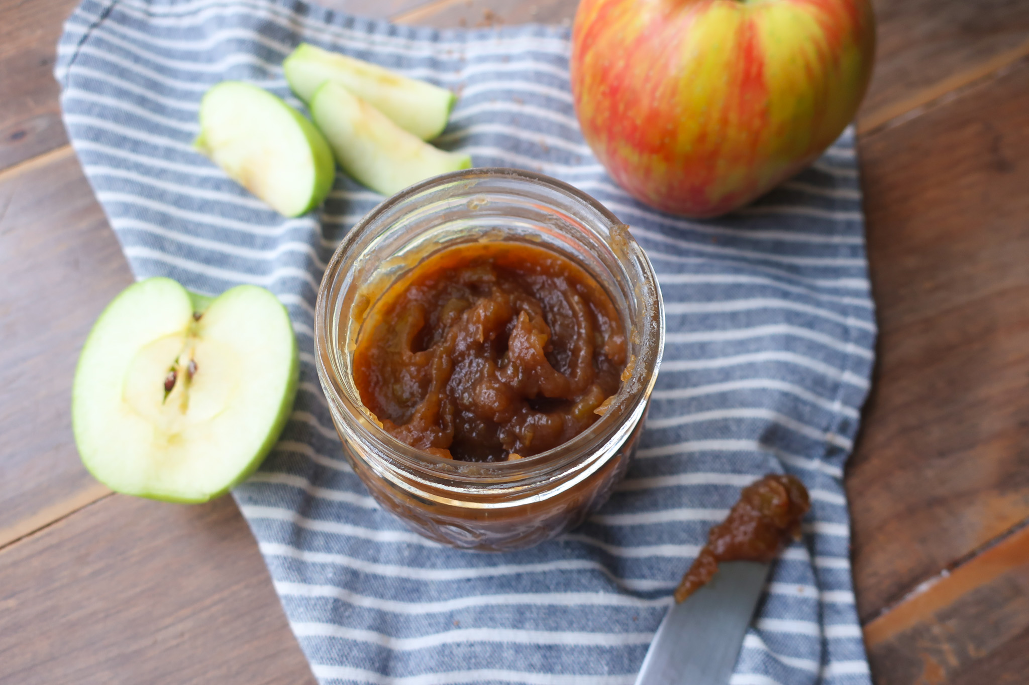 apple butter in jar on striped napkin with fresh apples