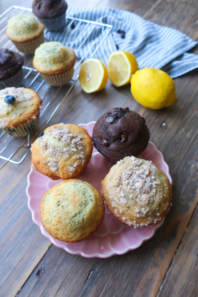 variety of muffins on a pink plate next to fresh fruit