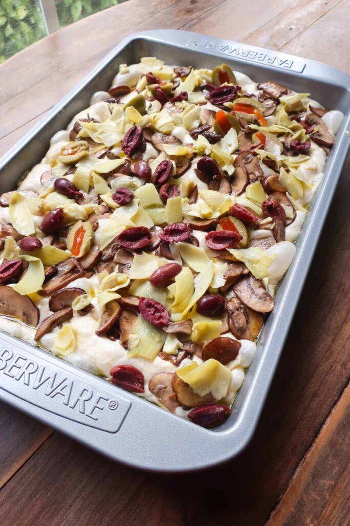 focaccia dough topped with olives artichokes and mushrooms in pan